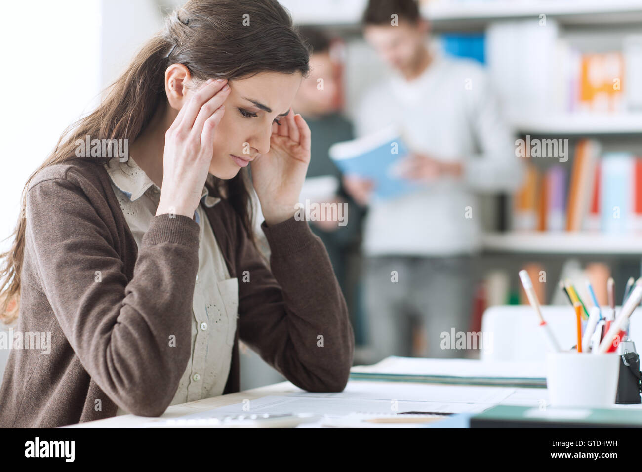 Giovane studentessa con cefalea, lei è seduta alla scrivania e di toccare la sua testa Foto Stock