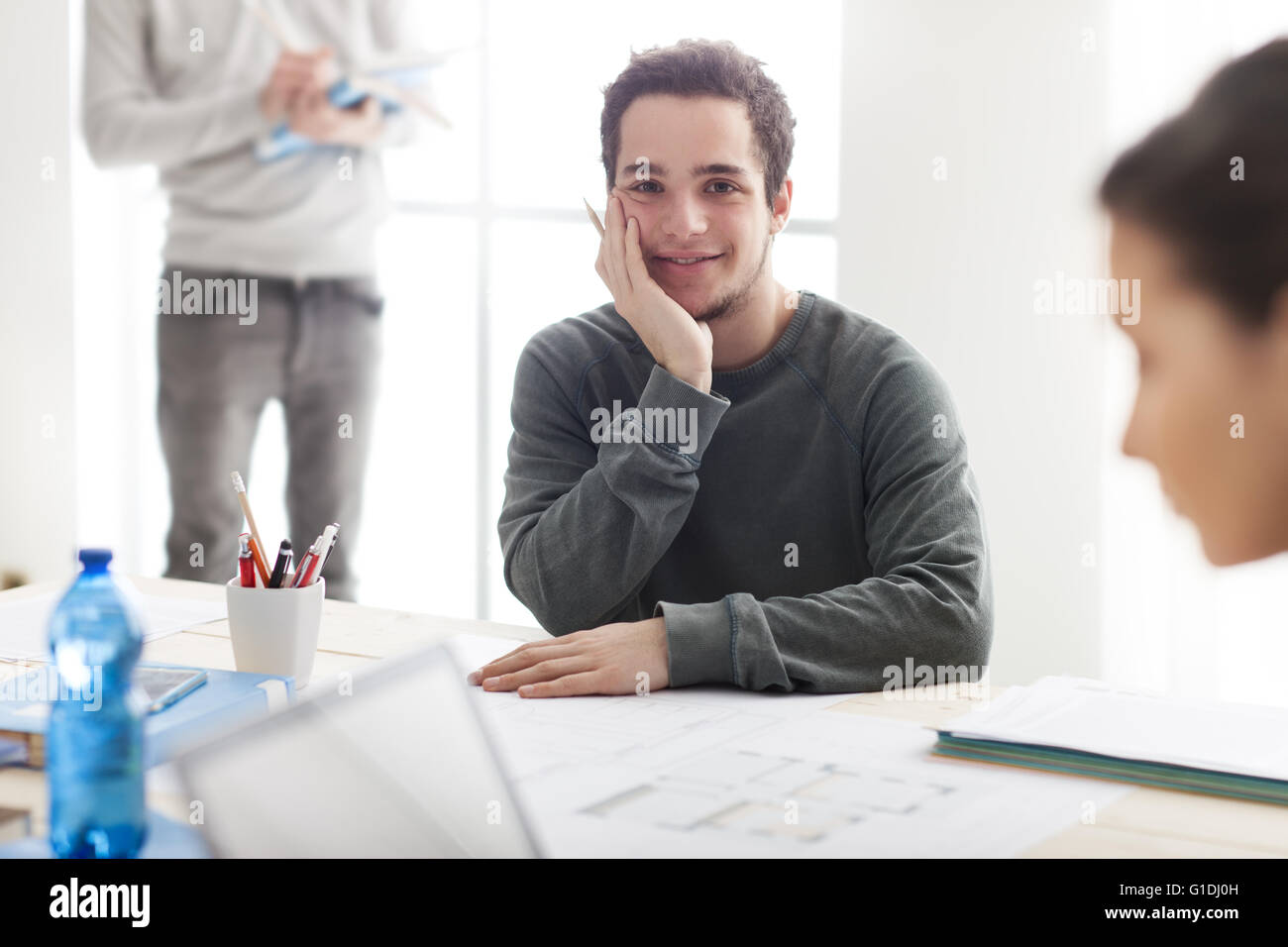 I ragazzi che studiano insieme alla scrivania, uno studente sorride alla telecamera e tenendo una matita, egli sta lavorando su un progetto scolastico Foto Stock