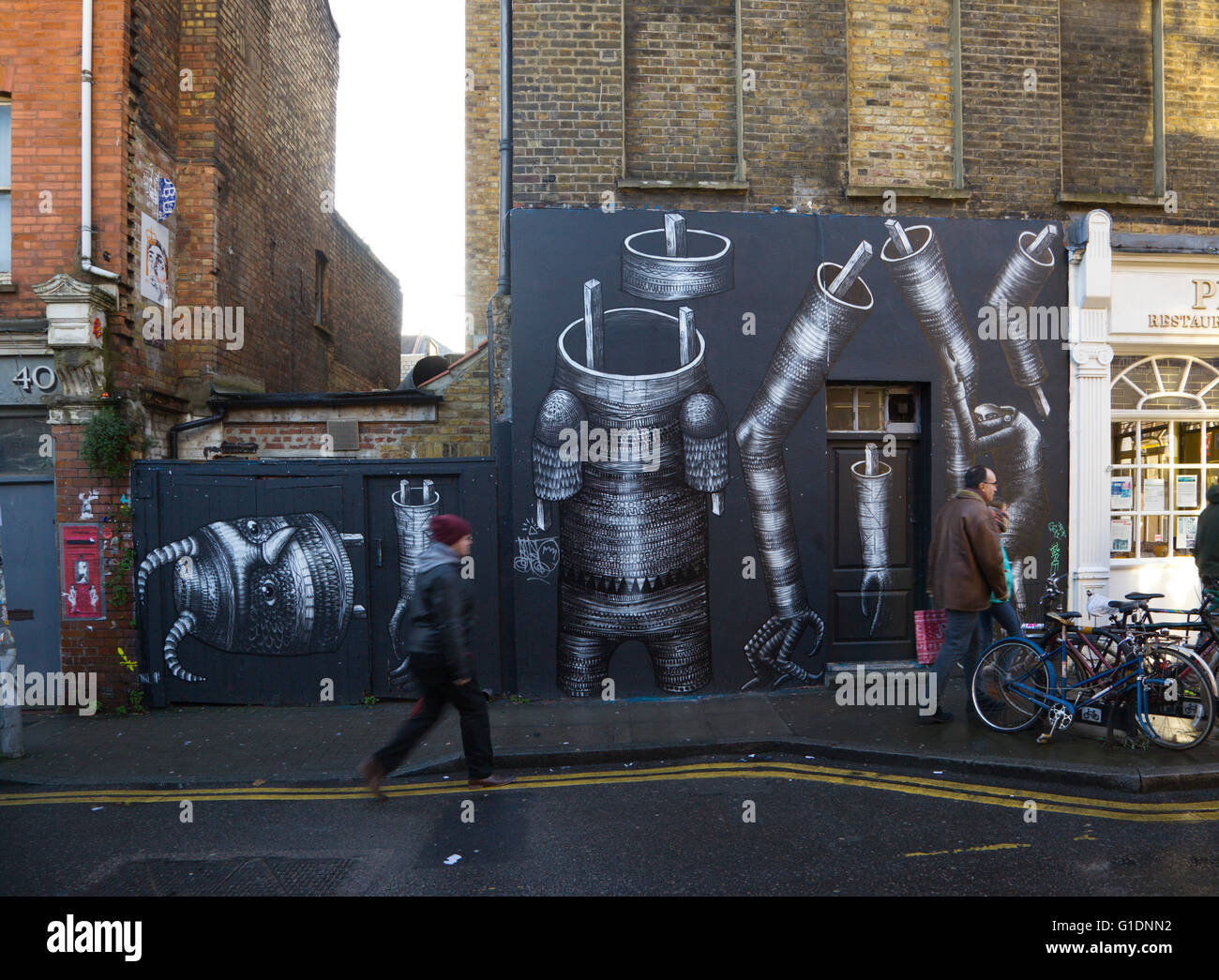 Scena in Hanbury Street, East London. La gente che camminava davanti a una grande arte di strada murale di robot parti dipinta su un muro. Foto Stock