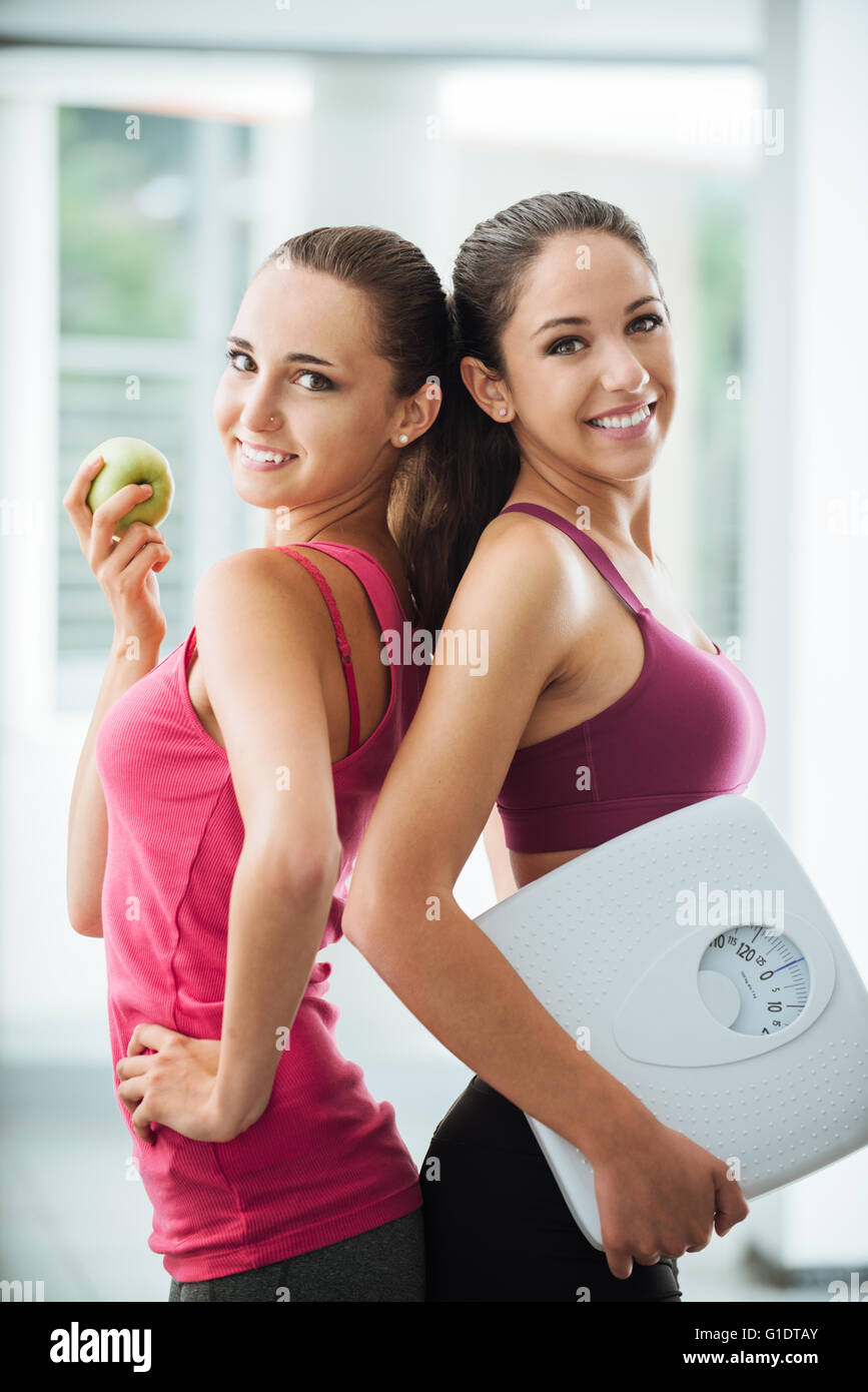 Felice ragazza adolescente amici in possesso di un Apple e una scala, essi sono in posa e sorridente alla fotocamera, fitness e perdita di peso concept Foto Stock