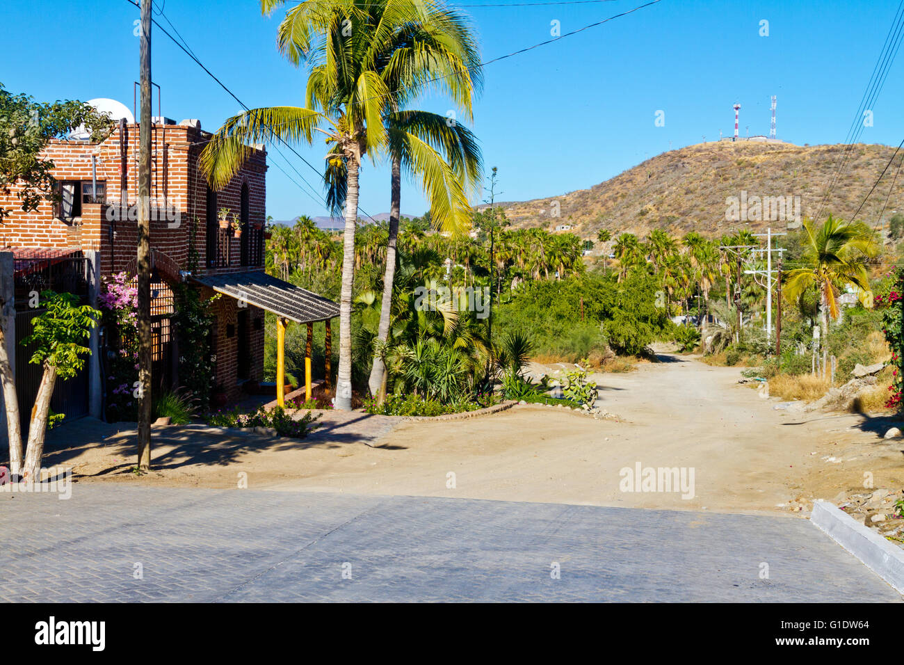 Vista di una strada in laterizio terminante in una strada sterrata che mostra un affascinante casa in mattoni rossi in Todos Santos, Baja, Messico. Foto Stock