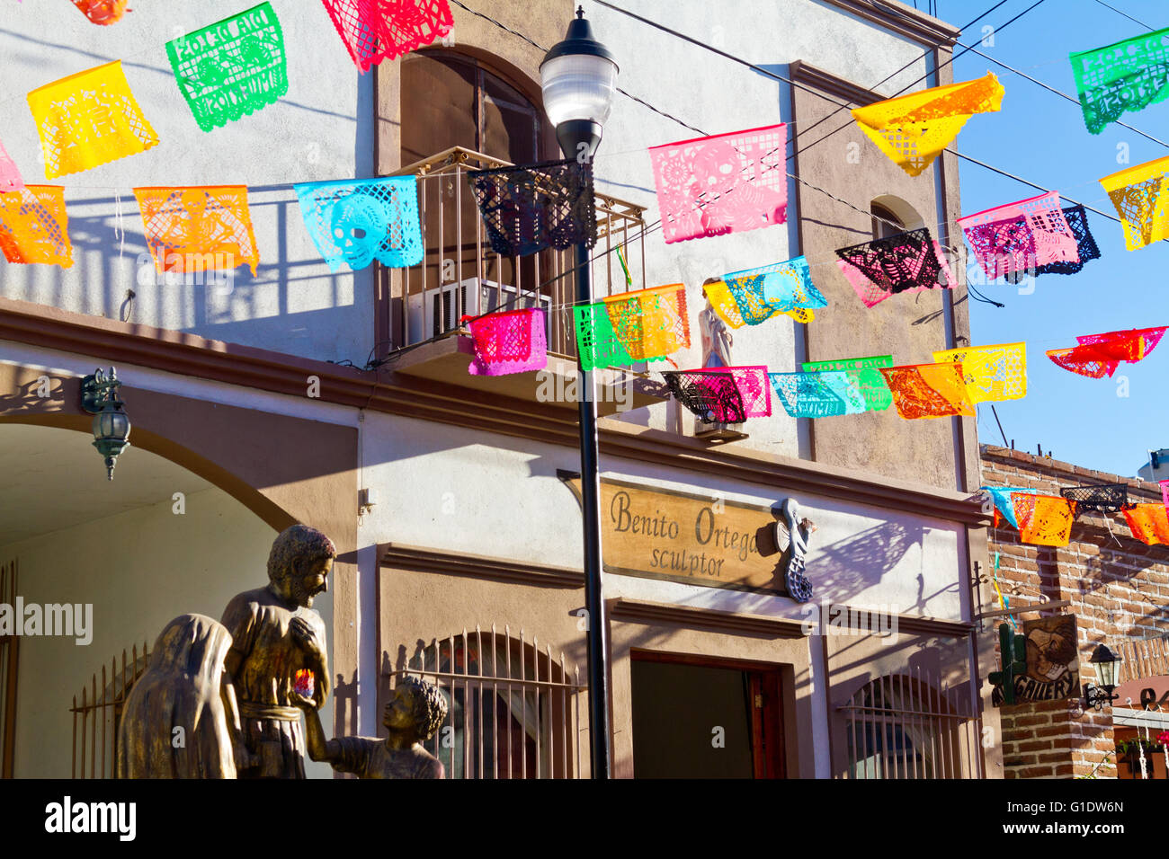Papel picados (bandiere di carta) decorare una strada a Todos Santos, Baja, Messico di fronte lo studio dello scultore Benito Ortega. Foto Stock