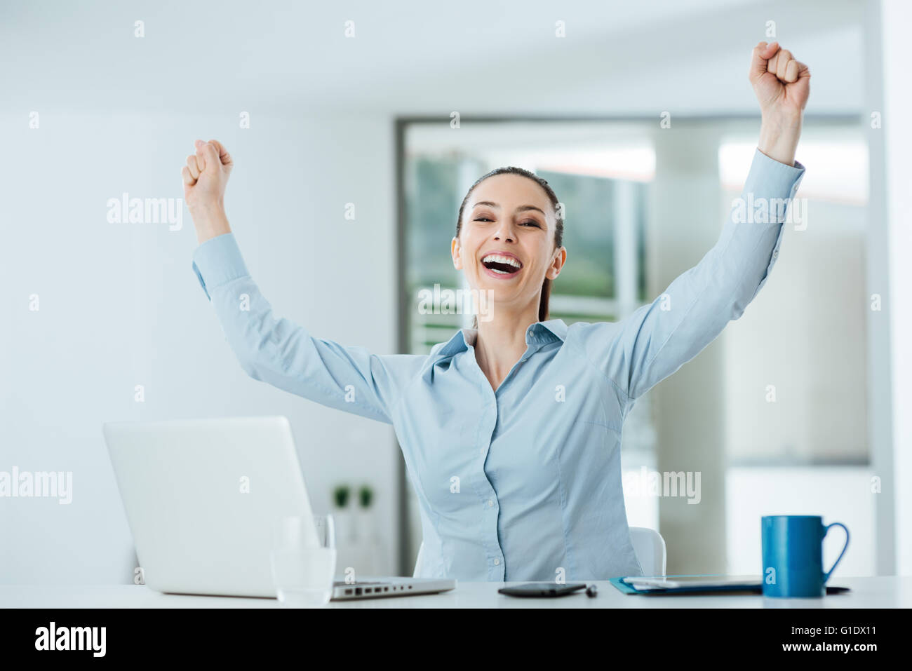 Successo imprenditrice allegro con i pugni sollevato seduto alla scrivania in ufficio, il raggiungimento e il concetto di soddisfazione Foto Stock