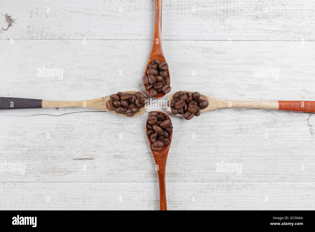 Quattro cucchiai di legno con chicchi di caffè tostati su bianco legno rustico. Vista da sopra con lo spazio di copia Foto Stock