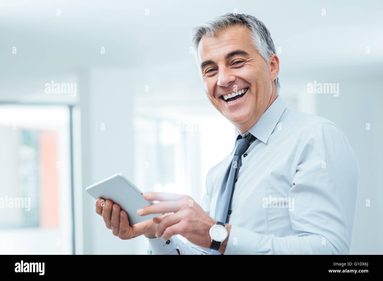 Sorridente imprenditore fiducioso guardando la fotocamera e con un digital tablet touch-screen Foto Stock