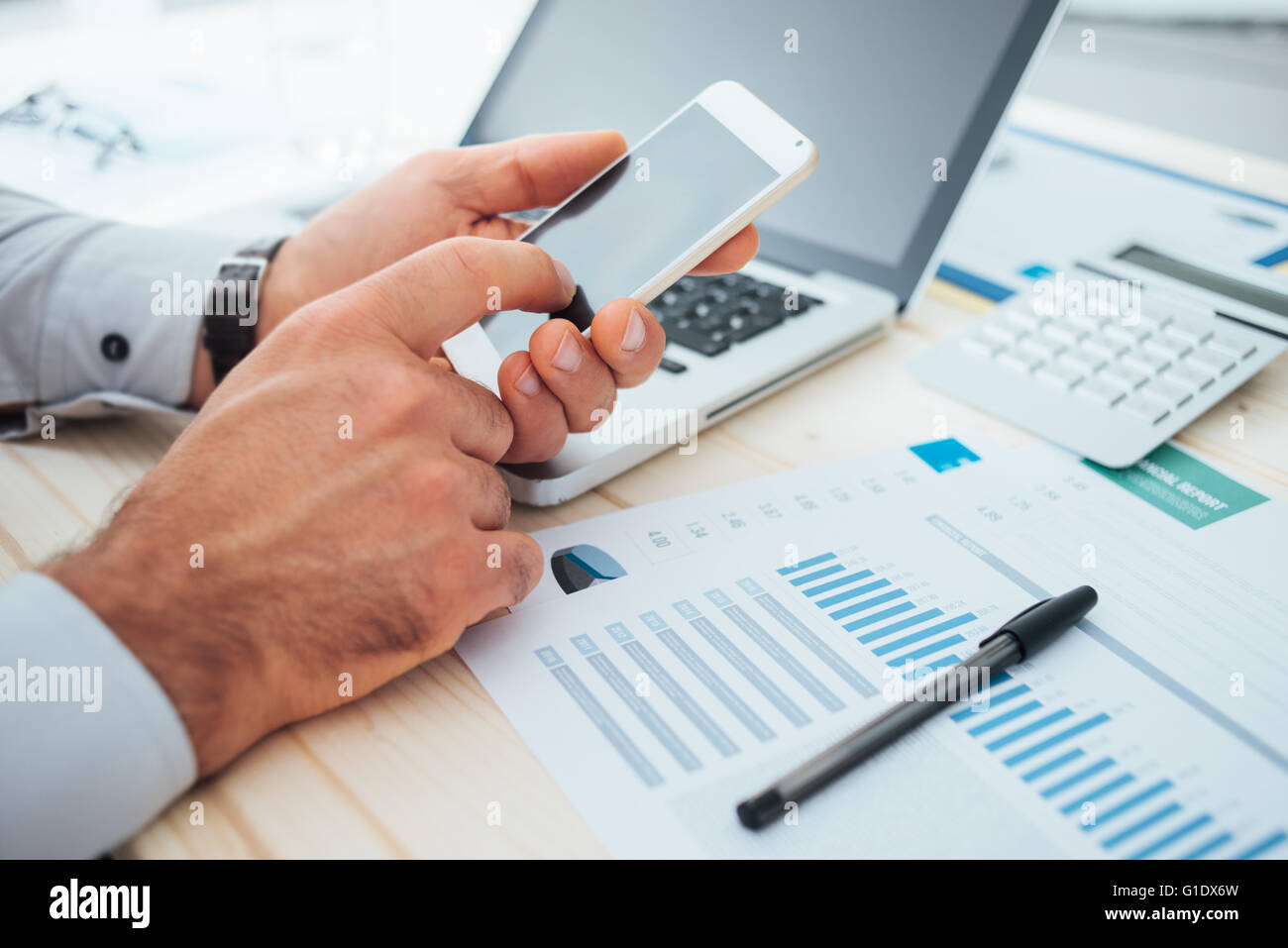 Imprenditore al desk utilizzando un'applicazione finanziaria sul suo smart phone e lavorare sulle relazioni e le mani vicino fino Foto Stock