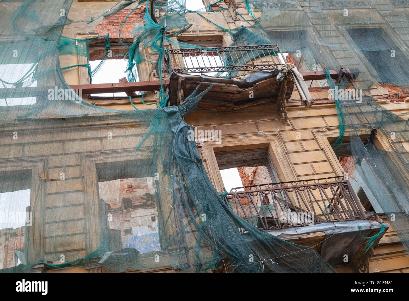 Vecchia casa vivente è in ricostruzione, facciata con balconi rotto è ricoperta di verde maglia di protezione Foto Stock