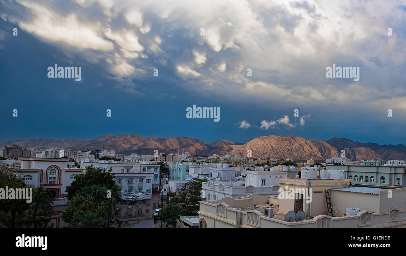 Pulire le montagne che riflette il sole serale con pioggia nuvole sopra e bagnato edifici della città e pozze di acqua in primo piano Foto Stock