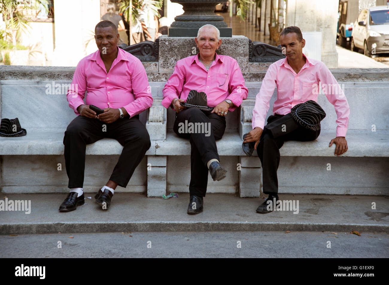 Tre cubani cantanti maschi vestito in rosa camicie e cappelli da cowboy a sedersi su una panchina nel centro di Avana Cuba Foto Stock