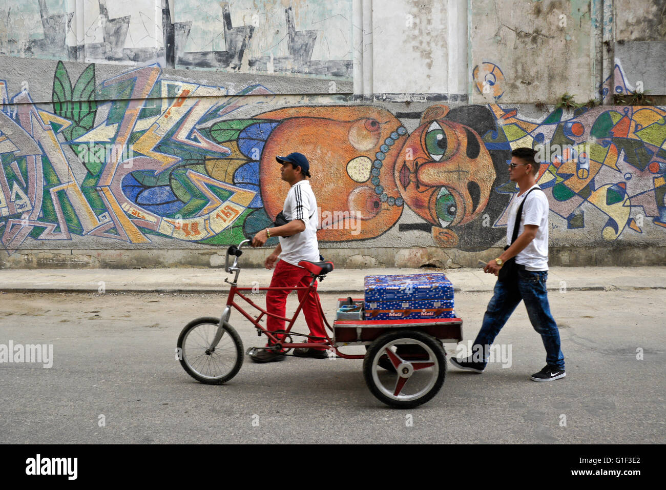 Gli uomini con la bicicletta carrello passando street murale di Havana, Cuba Foto Stock