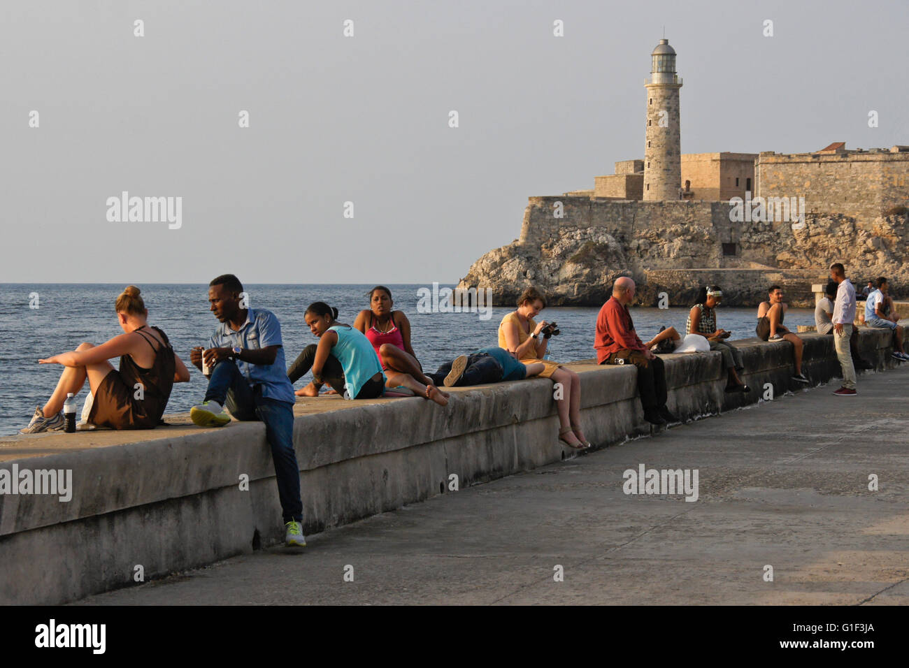 Habaneros rilassarsi sul Malecon parete sul mare nei pressi di Castillo de San Salvador de la Punta, Havana, Cuba Foto Stock