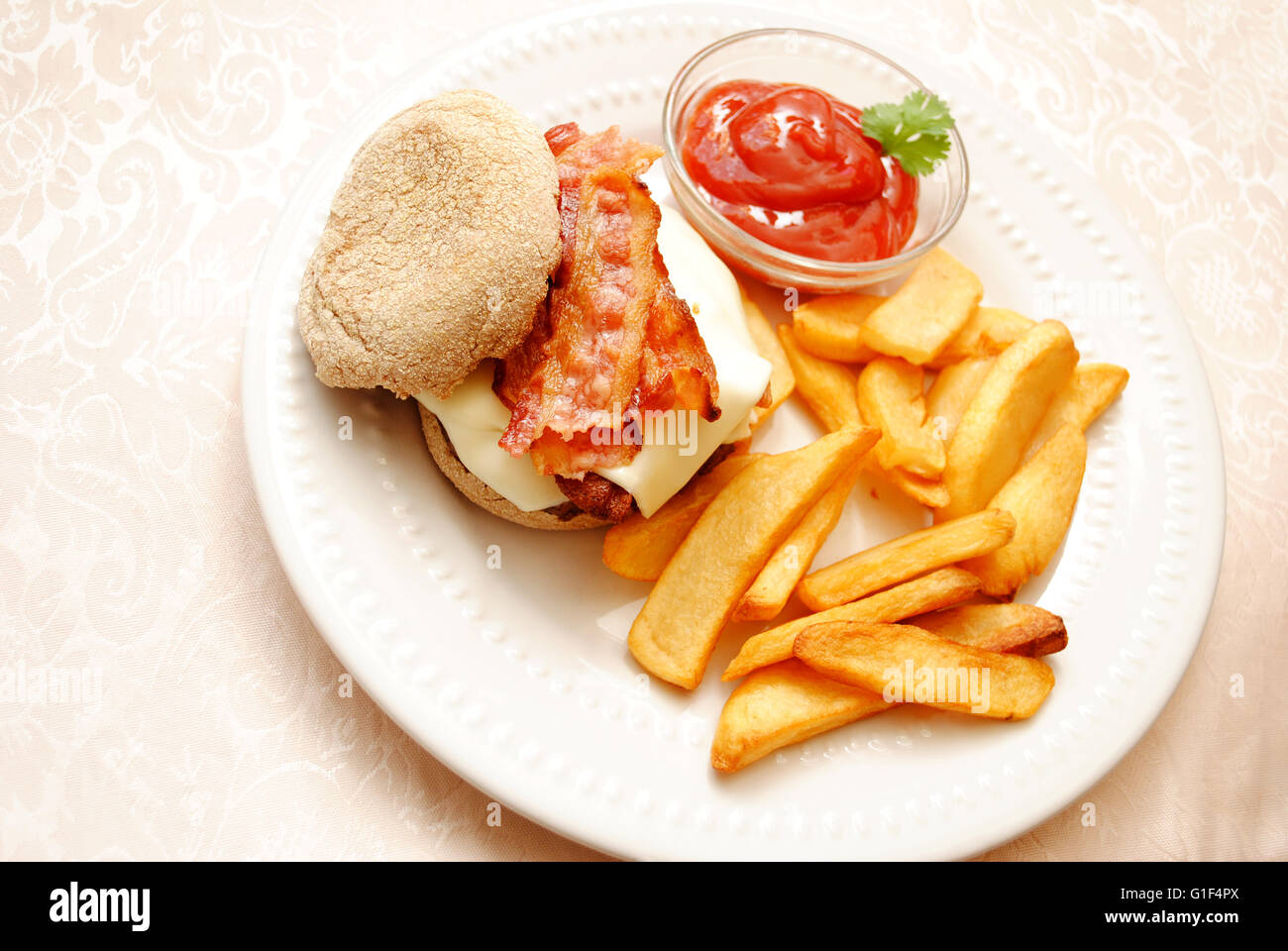 Bacon Cheeseburger servita su un grano muffin inglese con patate fritte Foto Stock
