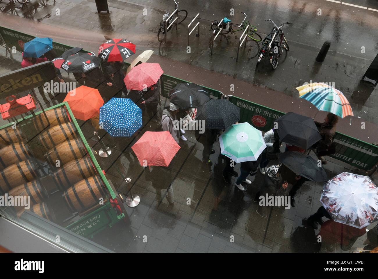Persone sotto la pioggia con ombrelloni in coda al di fuori del Museo Heineken edificio, Olanda, Amsterdam, Paesi Bassi. Foto Stock