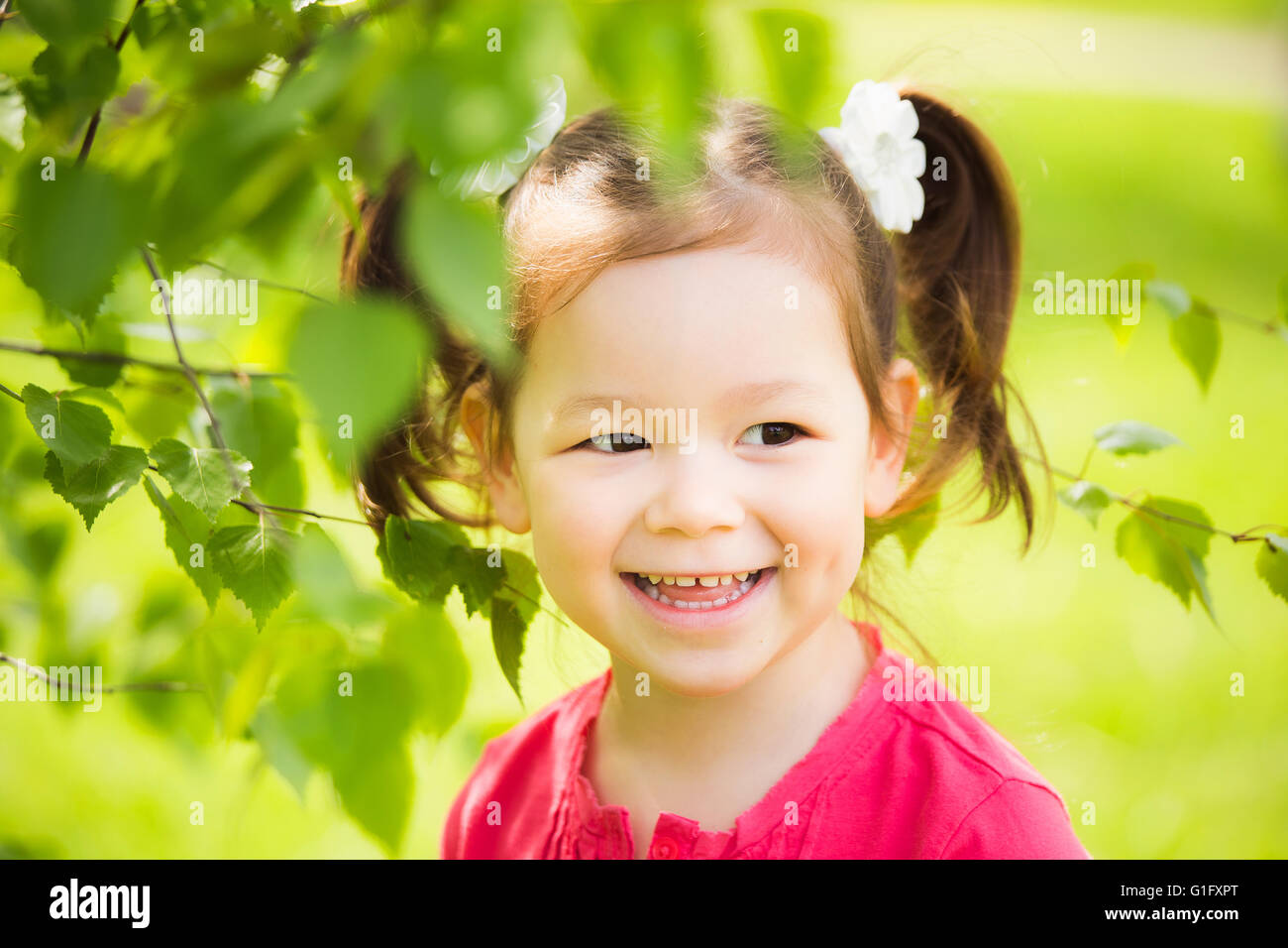 In prossimità della faccia del bambino di giocare a nascondino all'aperto nel parco. Bellissima bambina nascosto dietro un enorme albero in estate Foto Stock