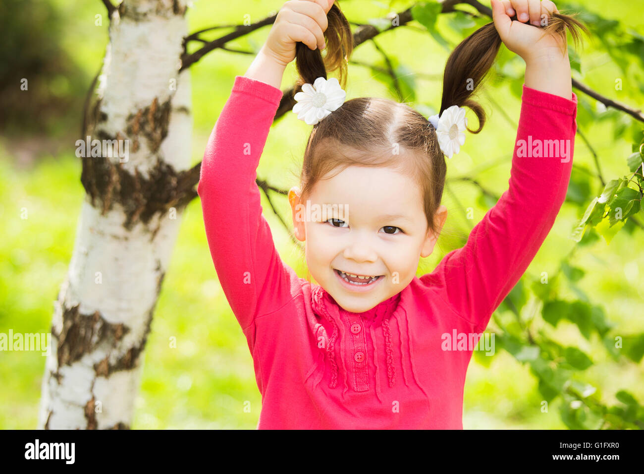 Closeup ritratto di divertenti piccole toddler girl. Ridendo bambino che gioca con i suoi capelli. Carefree allegro baby Foto Stock