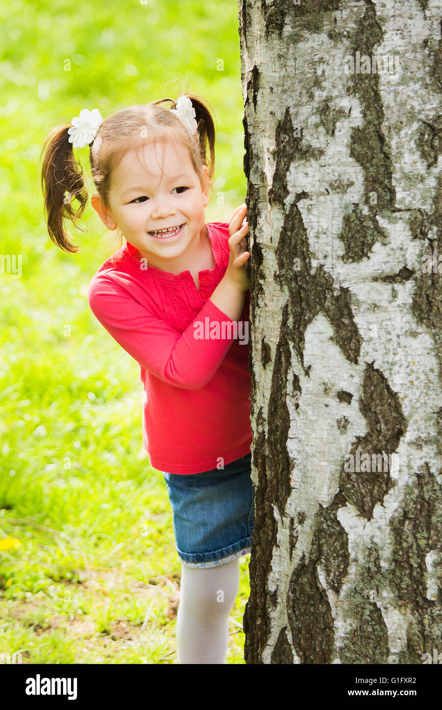 Bambini che giocano a nascondino all'aperto nel parco. Bellissima bambina nascosto dietro un enorme albero in primavera o estate giornata di sole Foto Stock