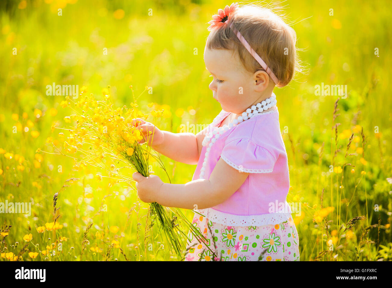 Piccolo, grazioso bambino che gioca da solo in primavera o in estate prato assolato pieno di fiori gialli. Allergy free baby per godersi la natura. Foto Stock