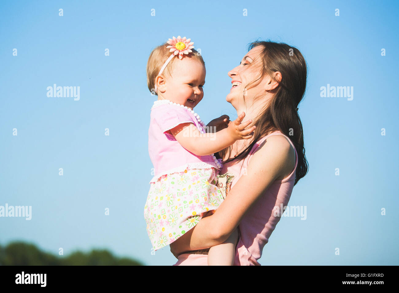 La mamma a giocare con il bambino al di fuori sulla soleggiata giornata calda. Ritratto di felice ridendo donna e bambina al cielo blu sullo sfondo. Mom h Foto Stock