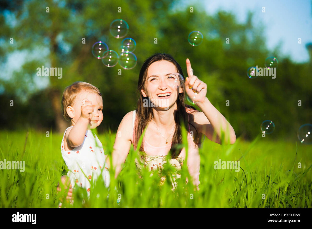 Famiglia giocando insieme all'esterno. Mamma e figlia piccola allegramente la cattura bolle di sapone. Ritratto di felice famiglia gioiosa Foto Stock