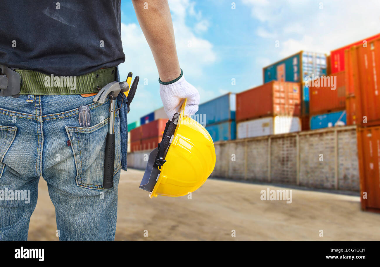 Ingegnere in possesso di un casco giallo per la sicurezza dei lavoratori sul background stock porta con contenitori. Foto Stock