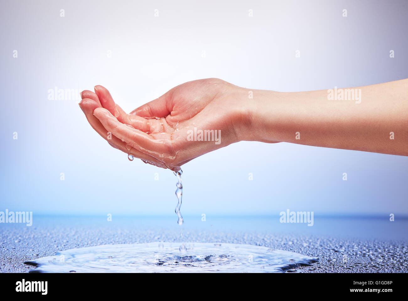 L'acqua che cade dalla mano womans su bianco e lo sfondo blu Foto Stock