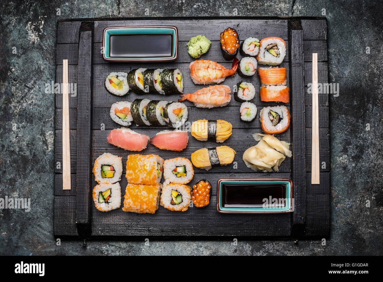 Sushi set: maki, nigiri , fuori rotoli servito con salsa di soia , zenzero sott'aceto e wasabi su legno scuro piastra , vista superiore Foto Stock