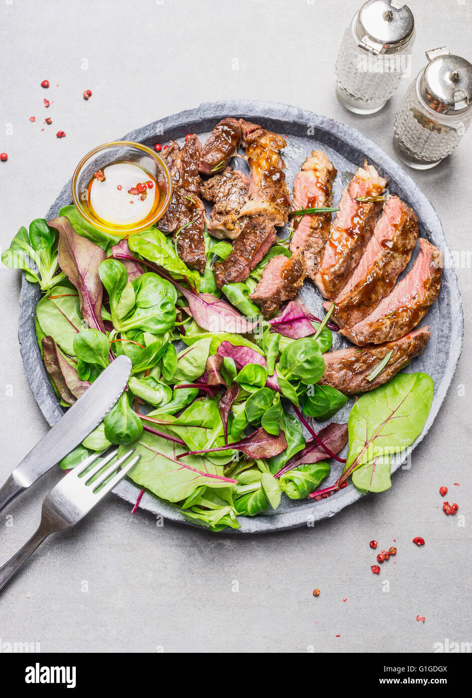 Fette di mezzo raro barbecue grigliate bistecca e insalata verde sulla lastra di pietra con posate, vista dall'alto Foto Stock