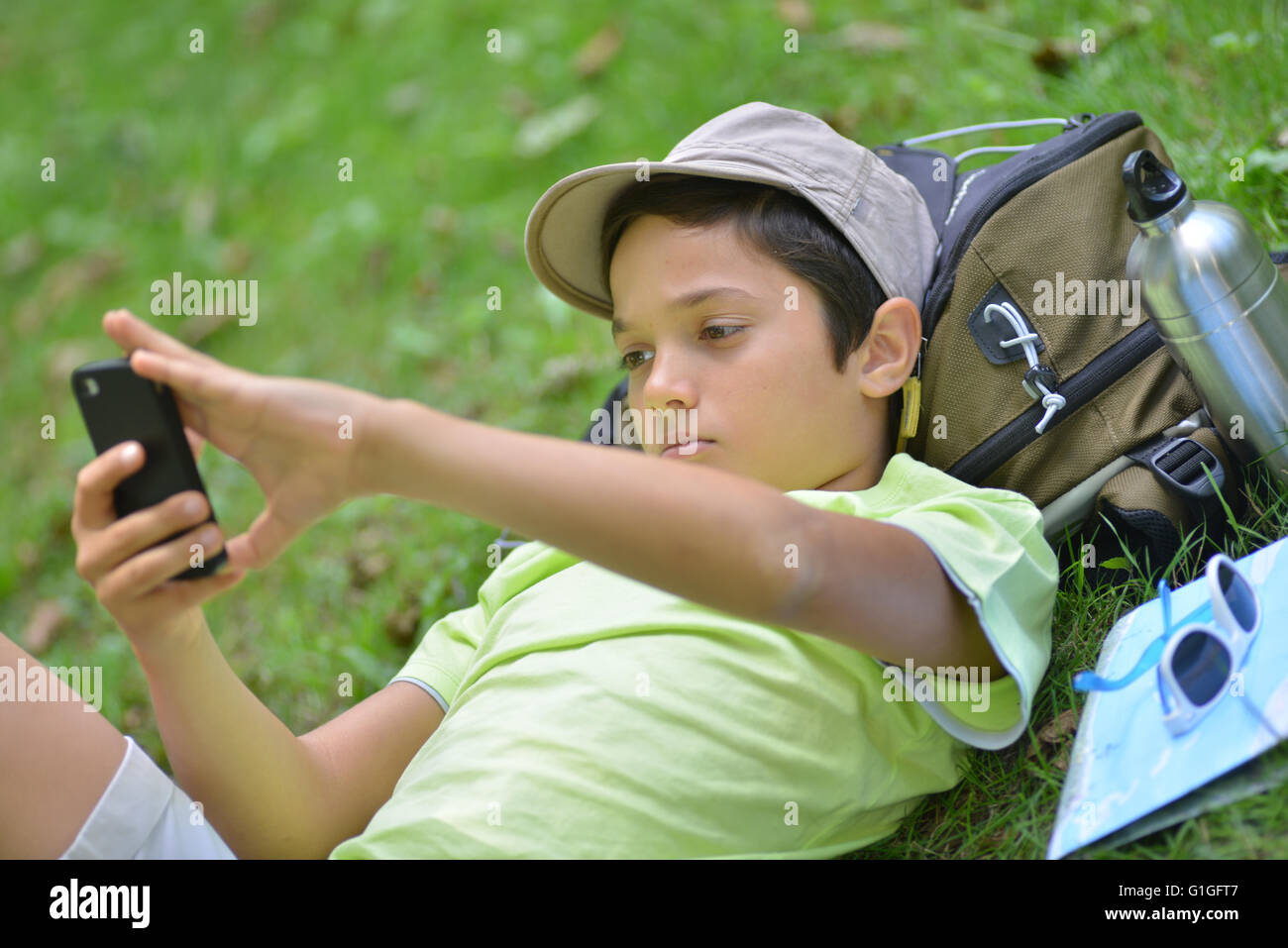 Ragazzo giovane giacente in erba facendo una Selfi con il suo telefono cellulare Foto Stock