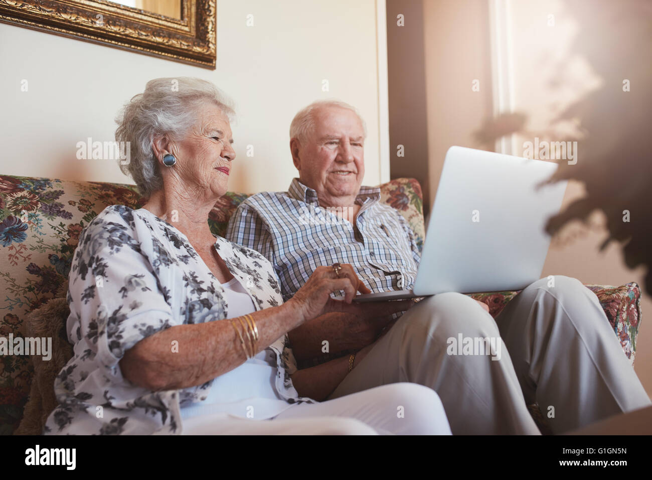 Coppia di anziani utilizzando computer portatile a casa. Senior l uomo e la donna seduta sul divano lavorando sul computer portatile. Foto Stock