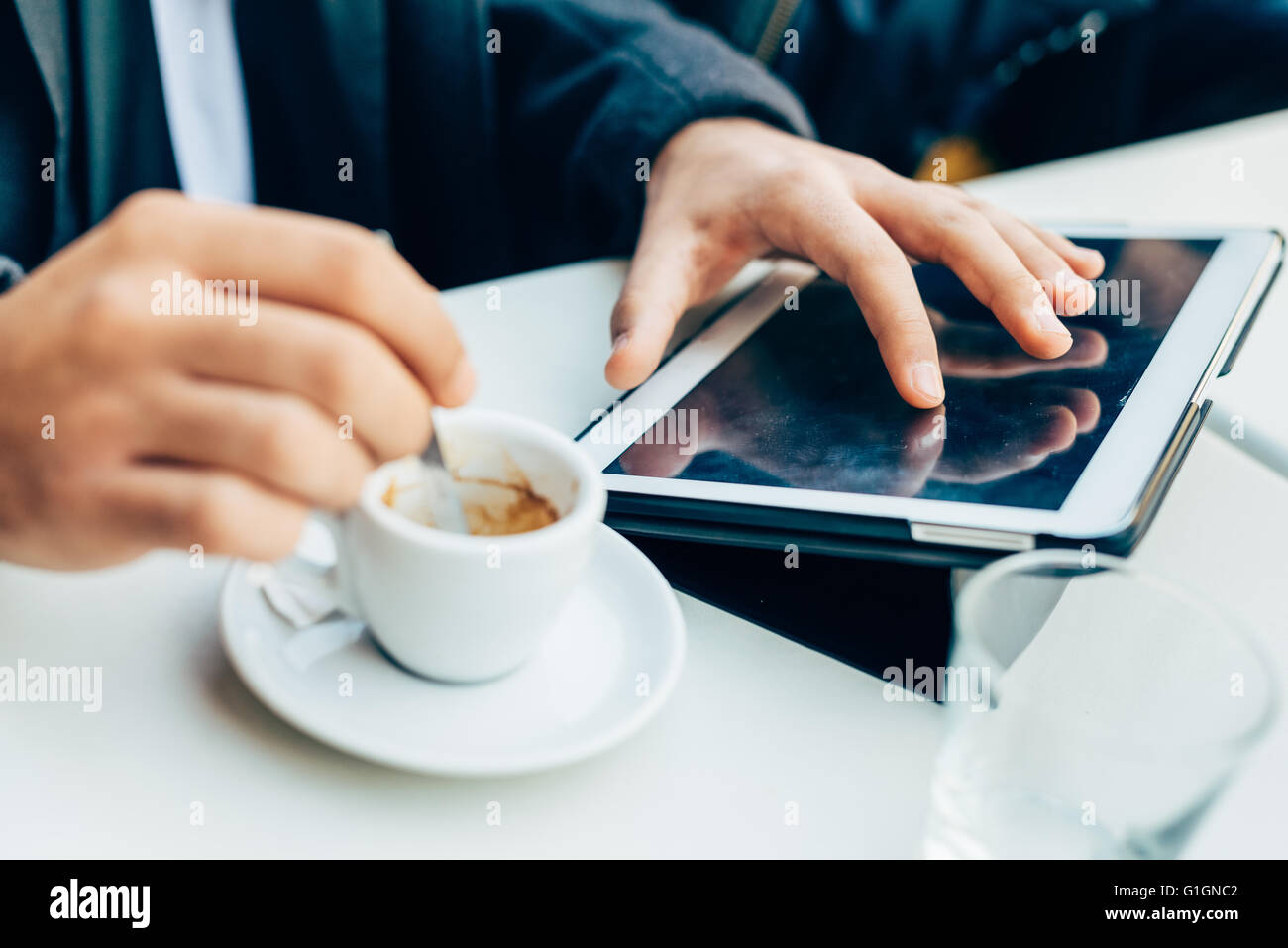 Chiudere fino alle mani del giovane imprenditore mescolando con un cucchiaio di una tazza di caffè e utilizzando la tavoletta, toccando lo schermo - tecnologia, lavoro, concetto di rottura Foto Stock