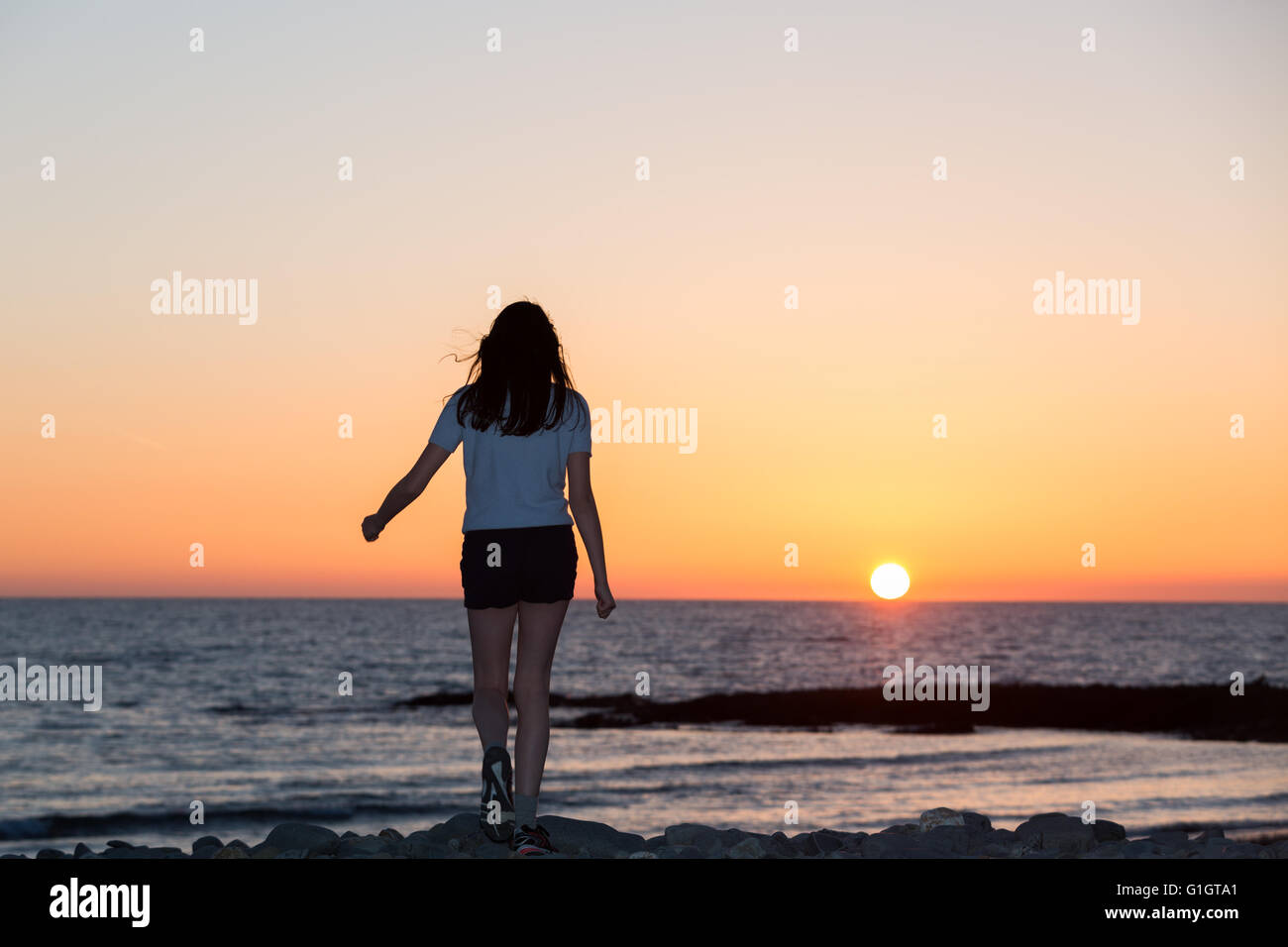 Una giovane ragazza su una spiaggia a piedi verso il tramonto. Credito: Ian Jones/Alamy Live News Foto Stock