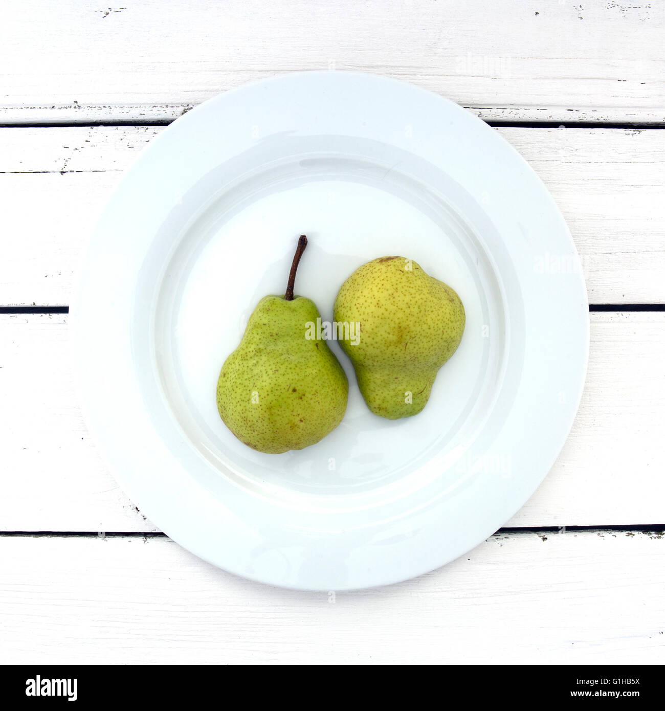 Due metà di pera su una piastra bianca su un retro bianco sullo sfondo di legno Foto Stock