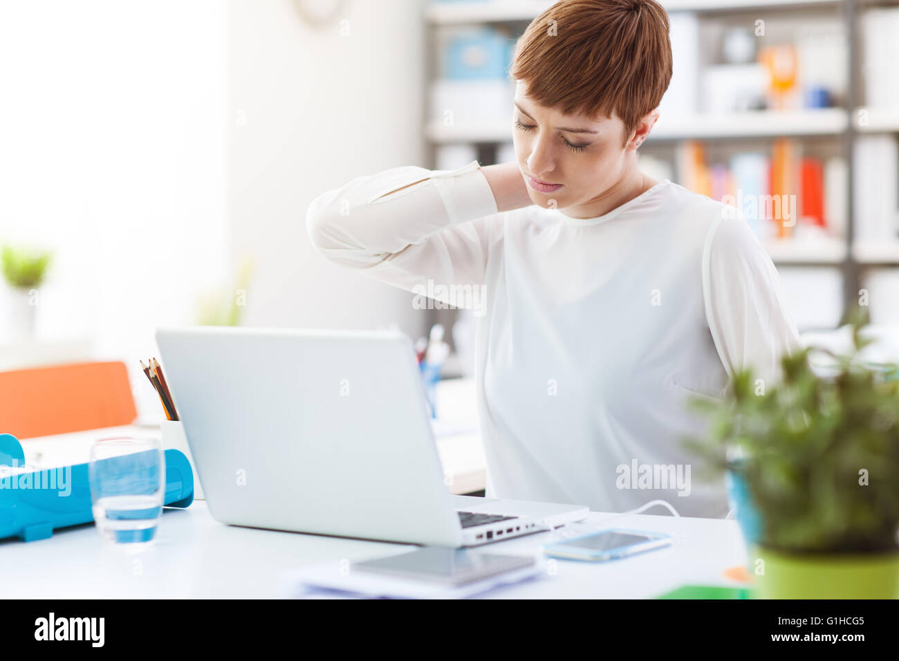 Lavoratore di ufficio seduti alla scrivania e toccando il suo indietro, sta avendo un dolore al collo Foto Stock
