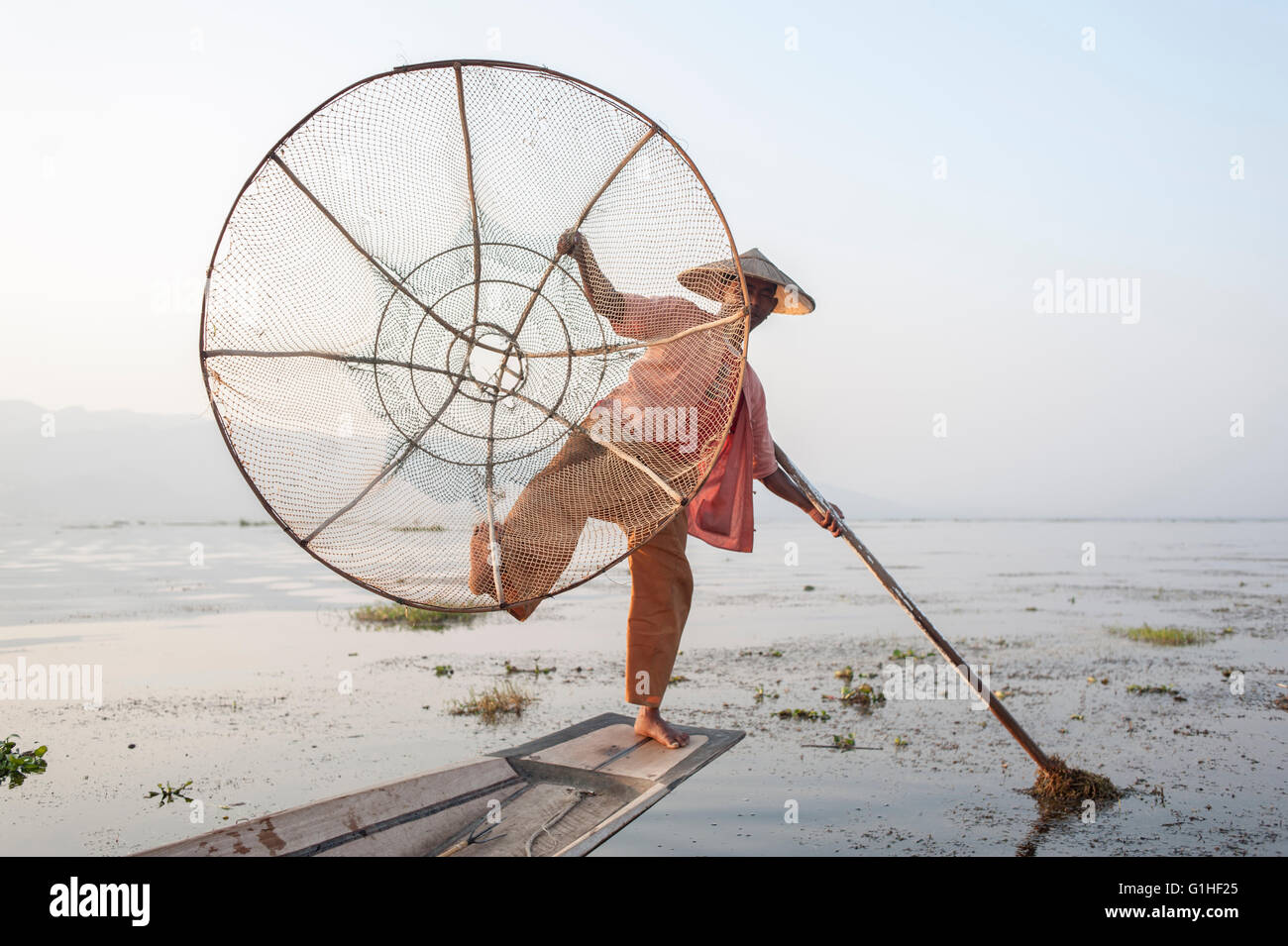 Pescatore tradizionale birmano con rete e pala singola da parte della minoranza Intha sul lago Inle nel nord-est di Myanmar, Birmania in Asia. Foto Stock