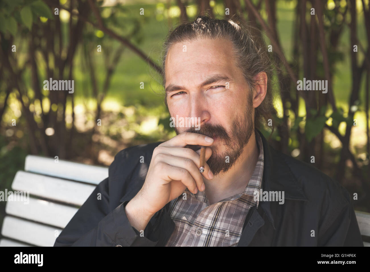 Uomo Barbuto di fumare il sigaro in estate park, outdoor ritratto con il fuoco selettivo Foto Stock