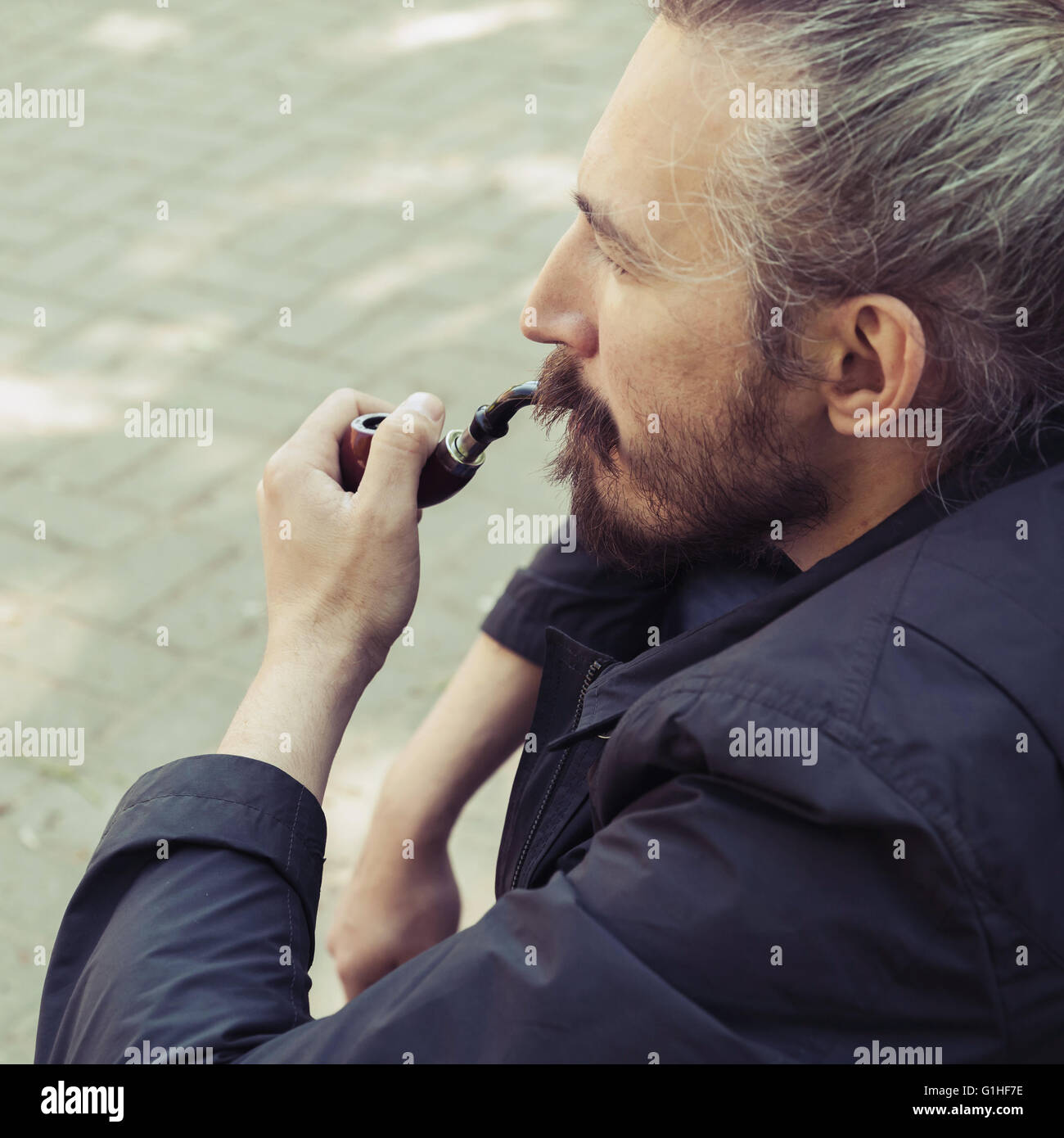 Uomo Barbuto fumatori, tubo quadrato ritratto all'aperto con il fuoco selettivo e vintage correzione tonale filtro foto, vecchio stile effe Foto Stock