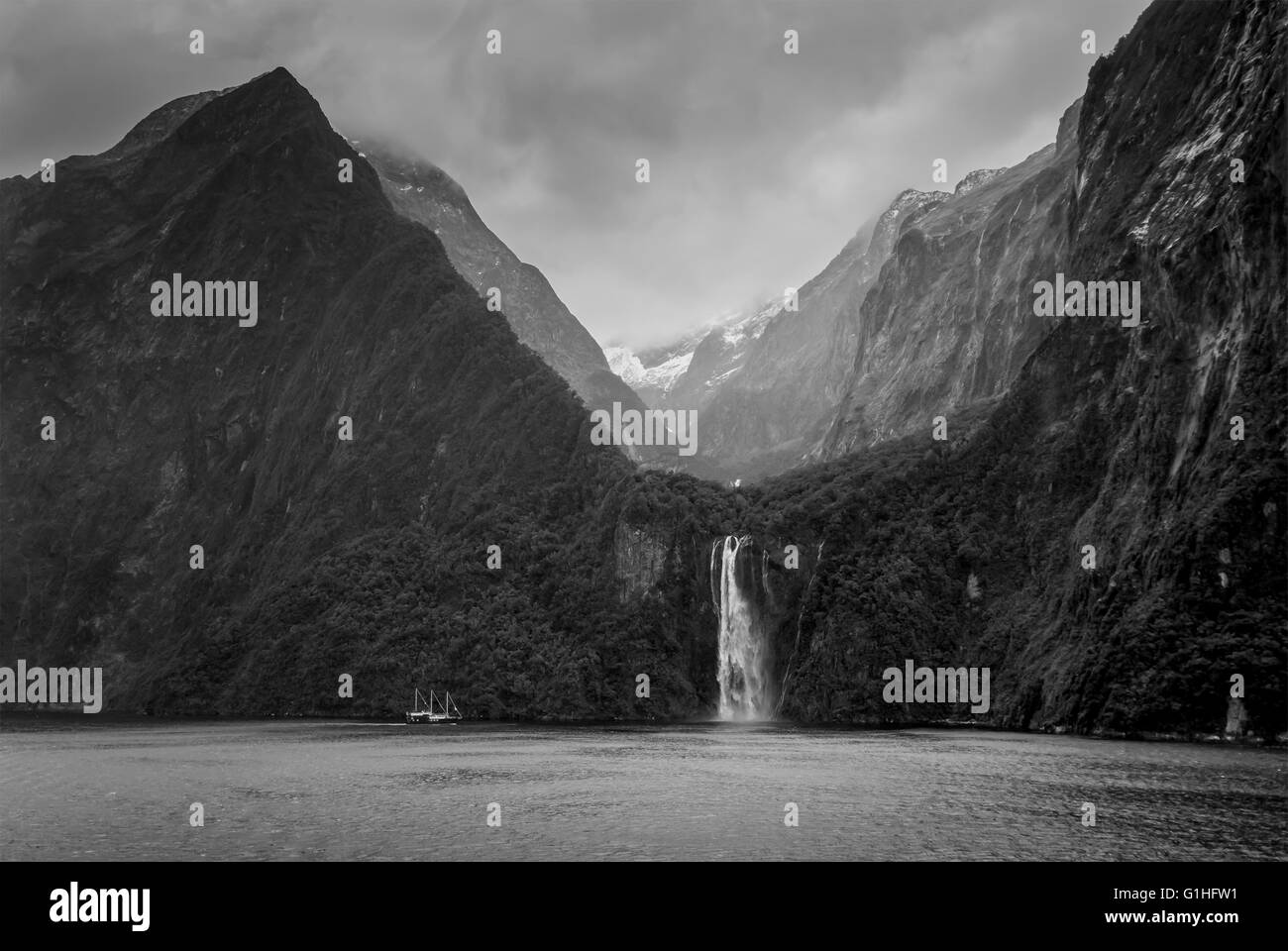 Nave vicino a cascata a Milford Sound Fjord in condizioni di tempo piovoso e drammatici sky - Isola del Sud della Nuova Zelanda - bianco e nero Foto Stock