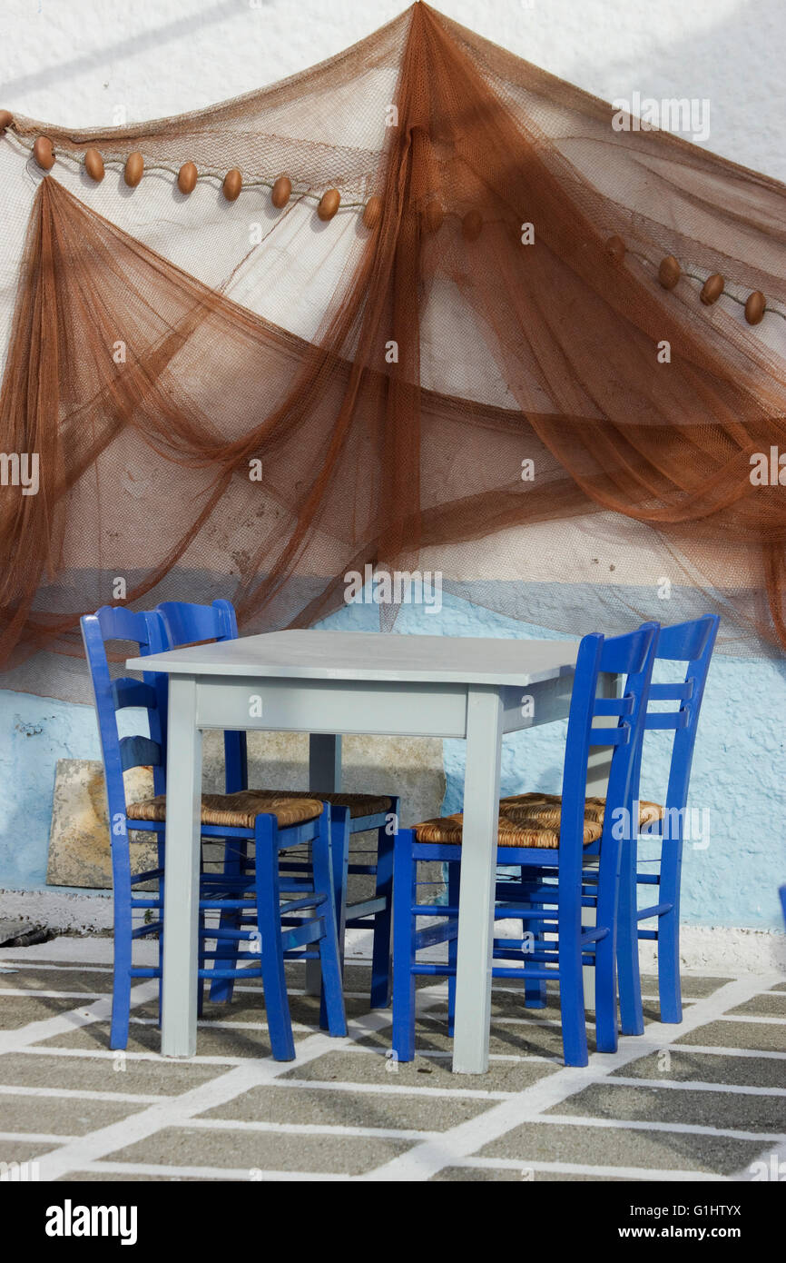 Set di sedie blu e ciano vuota taverna tavolo sul pavimento a scacchi & appendere le reti da pesca la decorazione parietale.Mirina, Limnos Grecia. Foto Stock