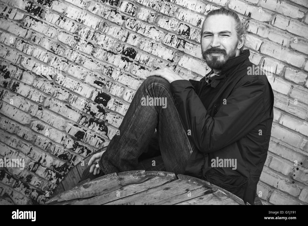 Outdoor Ritratto di giovane barbuto uomo asiatico in nero su grigio grungy urbano un muro di mattoni di sfondo, foto in bianco e nero Foto Stock