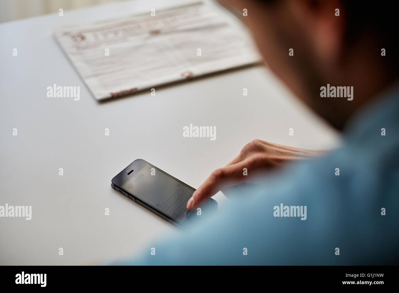 In camera è il ragazzo seduto a un tavolo bianco in una camicia blu e guardando il telefono Foto Stock