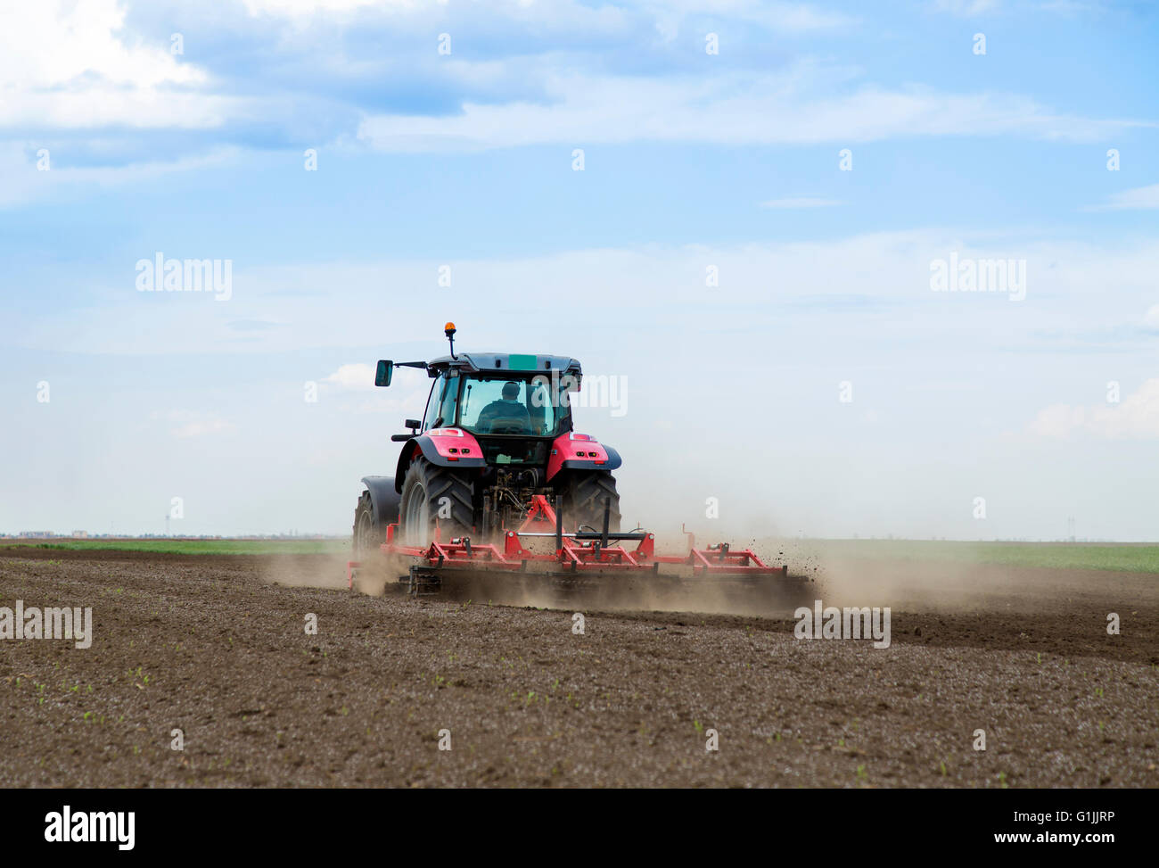 Trattore rosso azionato da un agricoltore la coltivazione di terreni a molla Foto Stock
