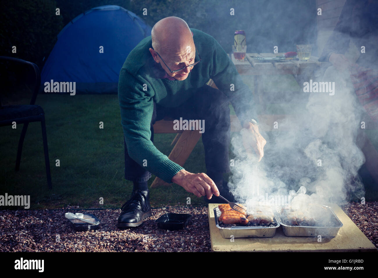 Un anziano uomo è la cottura della carne su un barbecue Foto Stock