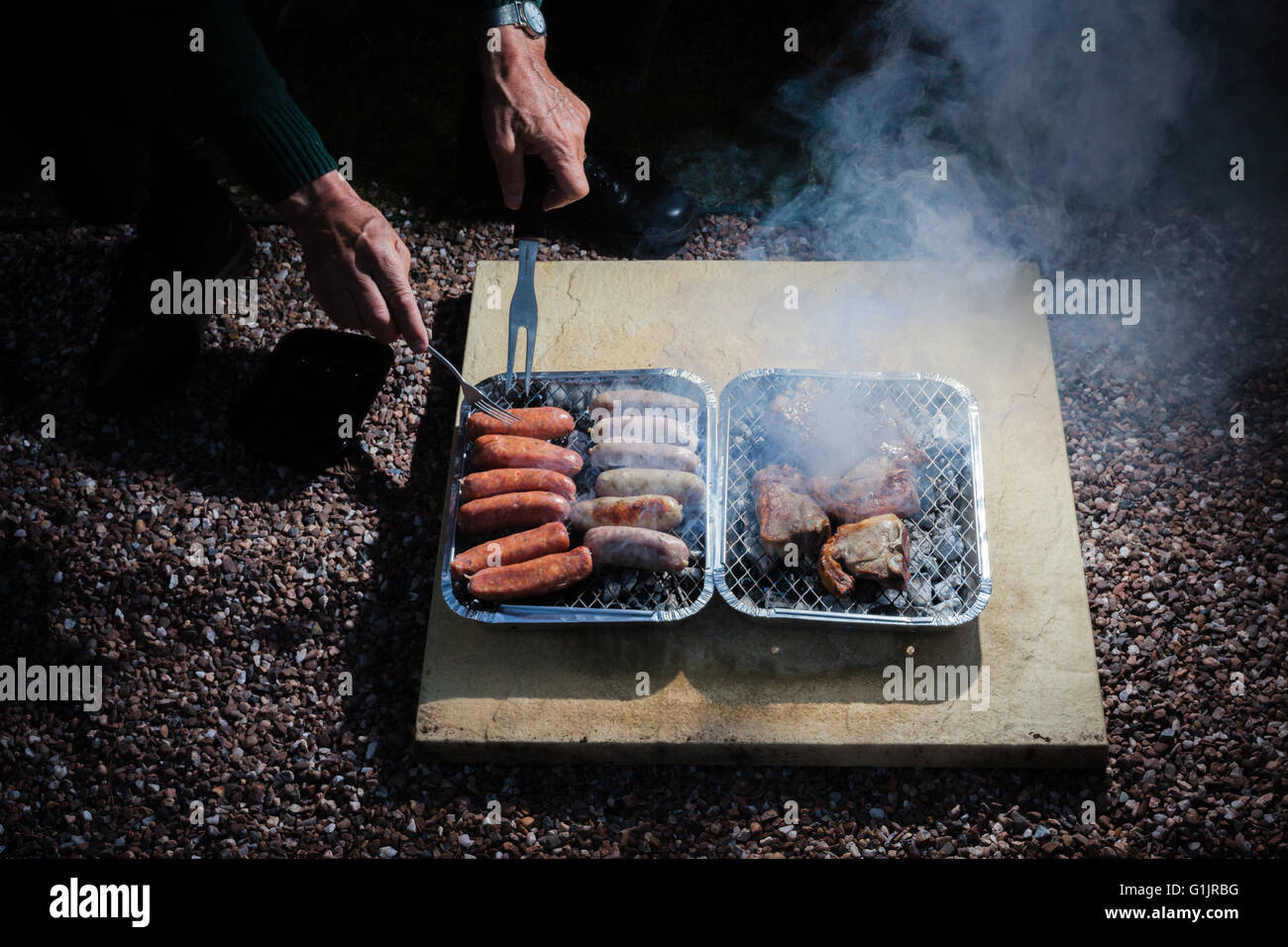 Primo piano sulle mani di un uomo anziano come egli sta partecipando a un barbecue esterno di notte Foto Stock