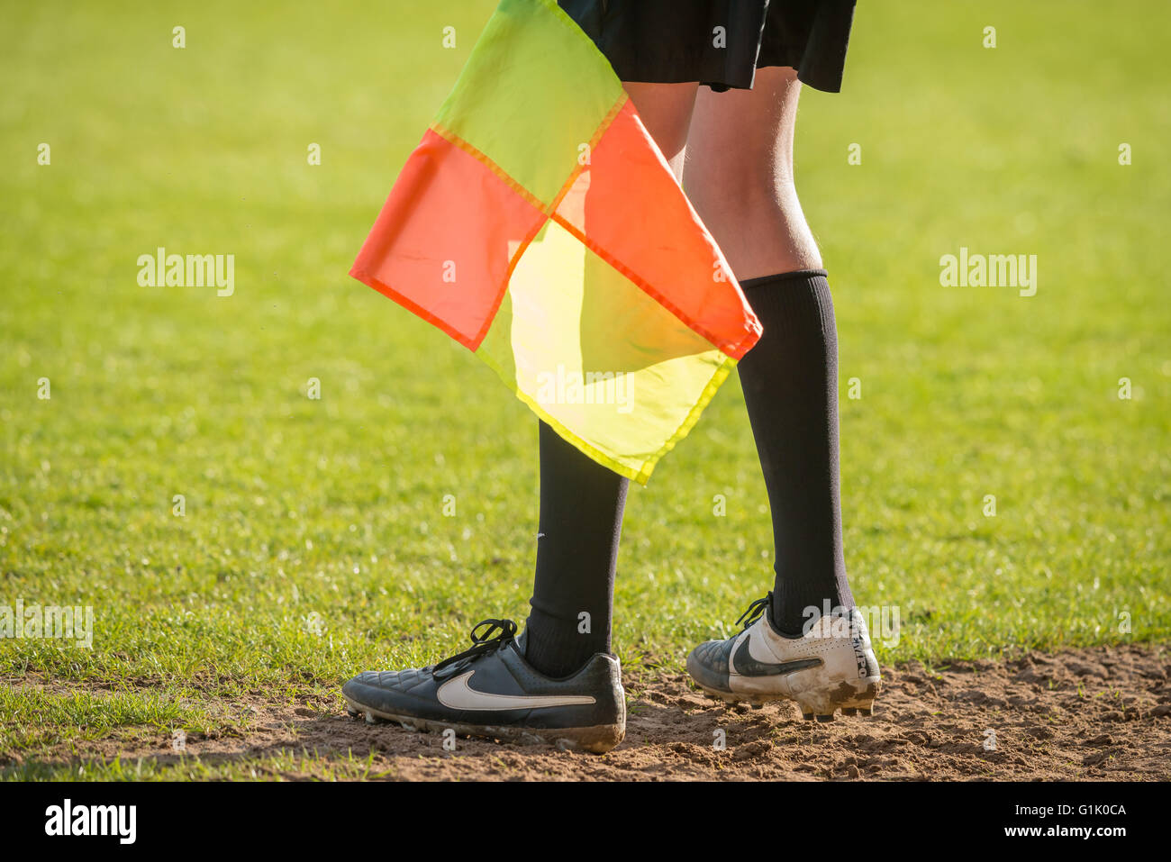 Un giovane aiuta per guardafili officiare sul perimetro durante una partita di calcio, close up di stivali e piedi con bandiera. Foto Stock