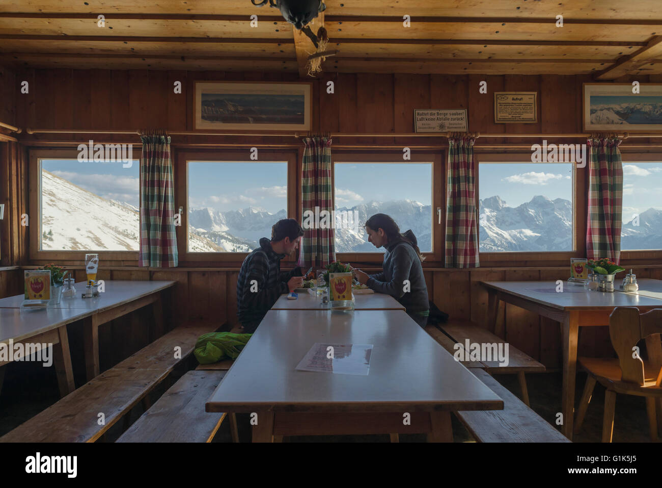 Coppia giovane mangiare la cena in baita Tölzer sala da pranzo con il panorama di innevate montagne Karwendel al tramonto,Tirol,Austria Foto Stock