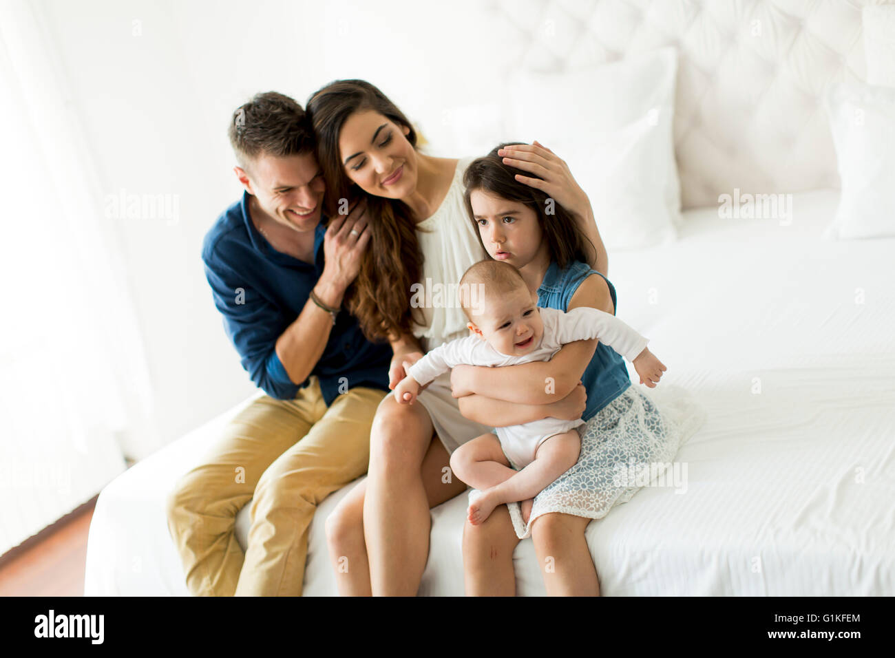 Felice giovani genitori seduti su un letto con una bambina e baby Foto Stock