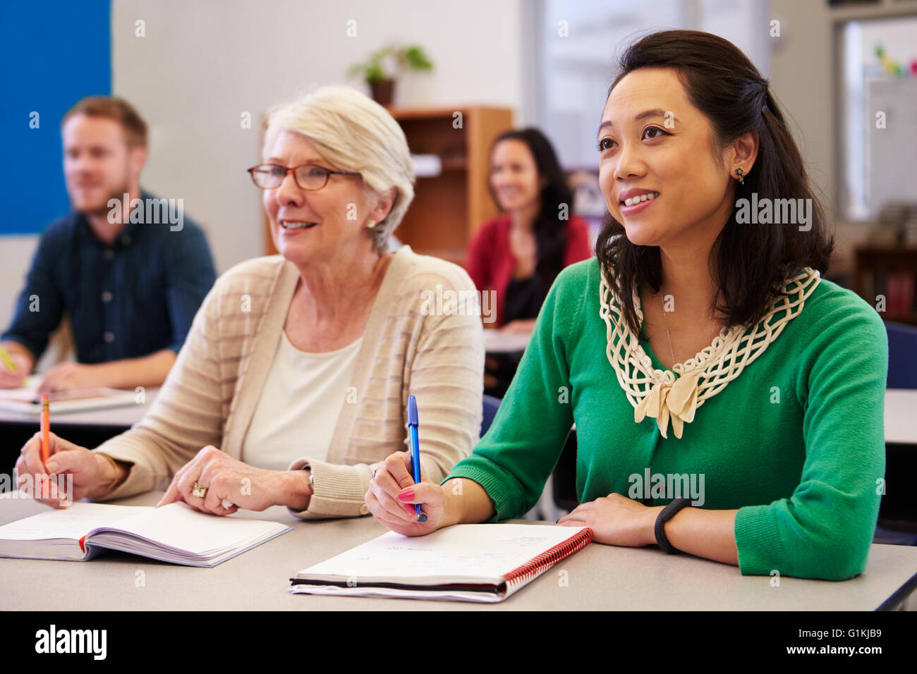 Due donne che condividono un banco in un adulto istruzione class look up Foto Stock