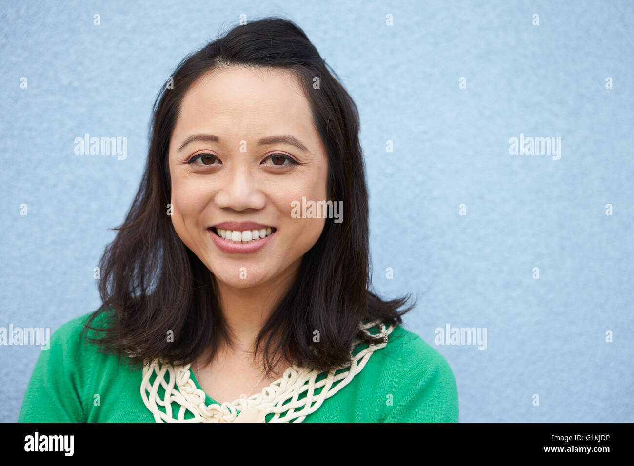 Ritratto di sorridere donna asiatica contro il muro grigio Foto Stock