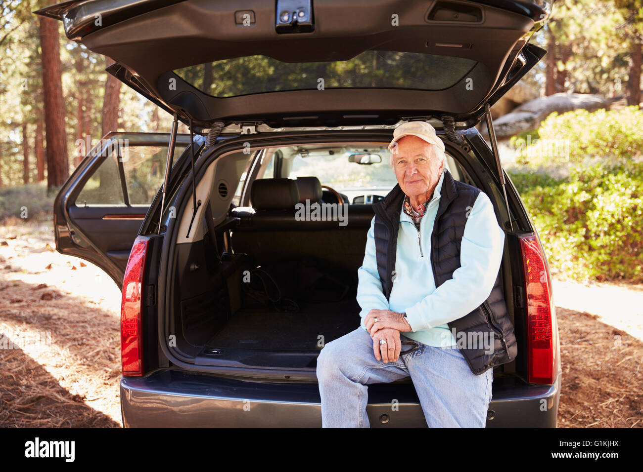 Senior uomo seduto nell'aprire il tronco di un automobile in una foresta Foto Stock