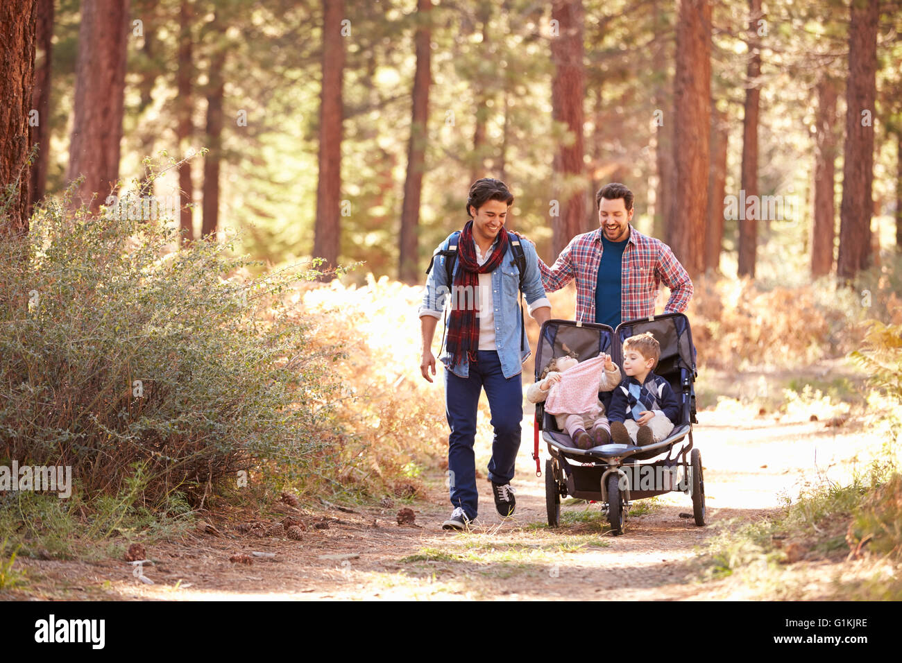 Gay maschio giovane spingendo i bambini in Buggy attraverso boschi Foto Stock